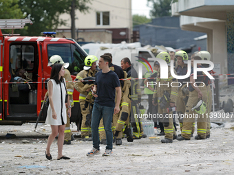 A man and woman are standing before rescue workers during a response effort to a Russian missile strike in the Solomianskyi district in Kyiv...