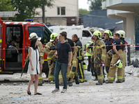 A man and woman are standing before rescue workers during a response effort to a Russian missile strike in the Solomianskyi district in Kyiv...