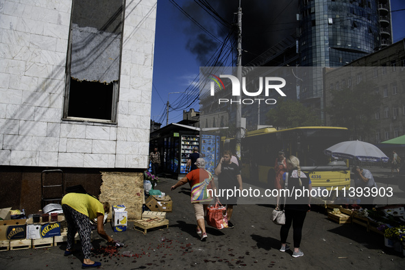 A woman is picking up scattered fruit with a burning building in the background that was damaged during a Russian missile strike in Kyiv, Uk...