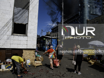 A woman is picking up scattered fruit with a burning building in the background that was damaged during a Russian missile strike in Kyiv, Uk...