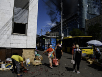 A woman is picking up scattered fruit with a burning building in the background that was damaged during a Russian missile strike in Kyiv, Uk...