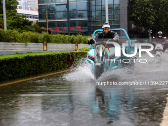 People are riding their bikes on a flooded road in Lianyun district, Lianyungang, China, on July 9, 2024. (