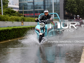 People are riding their bikes on a flooded road in Lianyun district, Lianyungang, China, on July 9, 2024. (