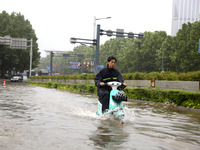 People are riding their bikes on a flooded road in Lianyun district, Lianyungang, China, on July 9, 2024. (