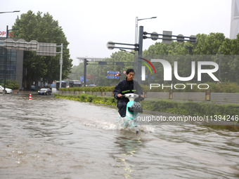 People are riding their bikes on a flooded road in Lianyun district, Lianyungang, China, on July 9, 2024. (