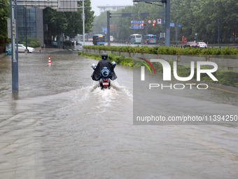 People are riding their bikes on a flooded road in Lianyun district, Lianyungang, China, on July 9, 2024. (