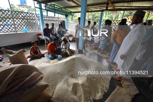 Flood-affected people are receiving food supplies at a relief center during flooding in a low-lying area in Nagaon District of Assam, India,...