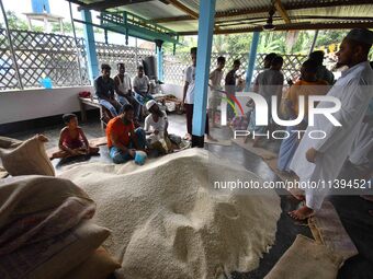 Flood-affected people are receiving food supplies at a relief center during flooding in a low-lying area in Nagaon District of Assam, India,...