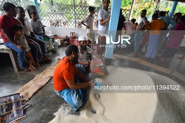 Flood-affected people are receiving food supplies at a relief center during flooding in a low-lying area in Nagaon District of Assam, India,...