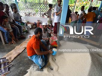 Flood-affected people are receiving food supplies at a relief center during flooding in a low-lying area in Nagaon District of Assam, India,...