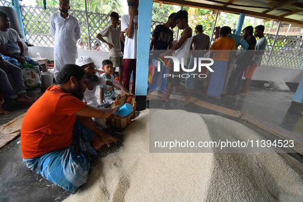 Flood-affected people are receiving food supplies at a relief center during flooding in a low-lying area in Nagaon District of Assam, India,...