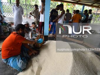 Flood-affected people are receiving food supplies at a relief center during flooding in a low-lying area in Nagaon District of Assam, India,...