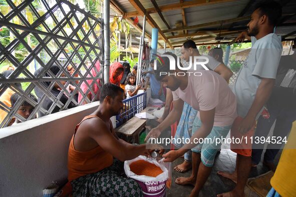 Flood-affected people are receiving food supplies at a relief center during flooding in a low-lying area in Nagaon District of Assam, India,...