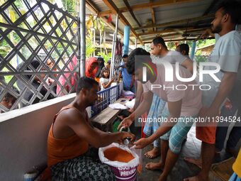 Flood-affected people are receiving food supplies at a relief center during flooding in a low-lying area in Nagaon District of Assam, India,...