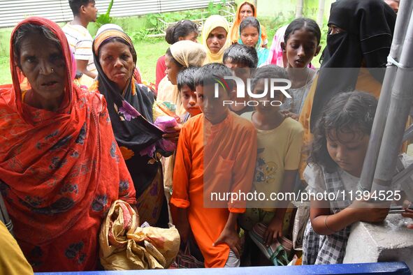 Flood-affected people are waiting in line to receive food supplies at a relief center during flooding in a low-lying area in Nagaon District...