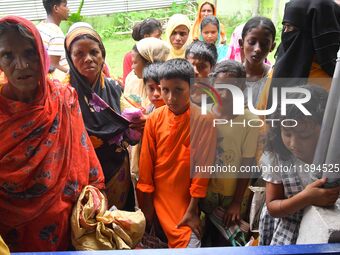 Flood-affected people are waiting in line to receive food supplies at a relief center during flooding in a low-lying area in Nagaon District...