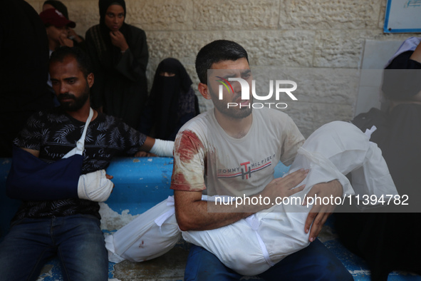 A Palestinian father is carrying the body of his son who was killed in an Israeli strike, amid the Israel-Hamas conflict, at Al-Aqsa Martyrs...