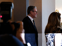 Partially illuminated by a camera flash, Keir Starmer, Prime Minister of the United Kingdom, departs a meeting between a bipartisan group of...