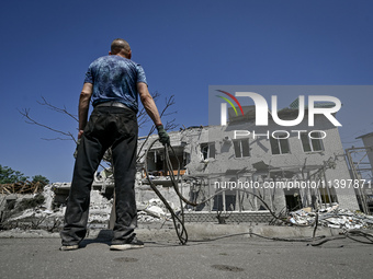 A man is holding a metal wire and looking at a building damaged by the July 8 Russian missile attack in Vilniansk, Zaporizhzhia region, sout...