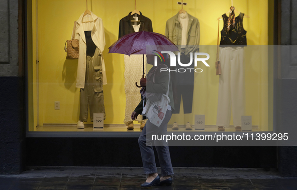 A woman is covering herself from the rain with an umbrella in the streets of Mexico City. 