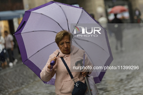 A woman is covering herself from the rain with an umbrella in the streets of Mexico City. 