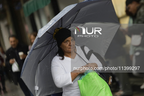 A woman is covering herself from the rain with an umbrella in the streets of Mexico City. 