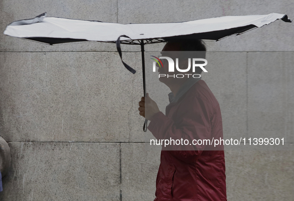 A man is covering himself from the rain with an umbrella in the streets of Mexico City. 