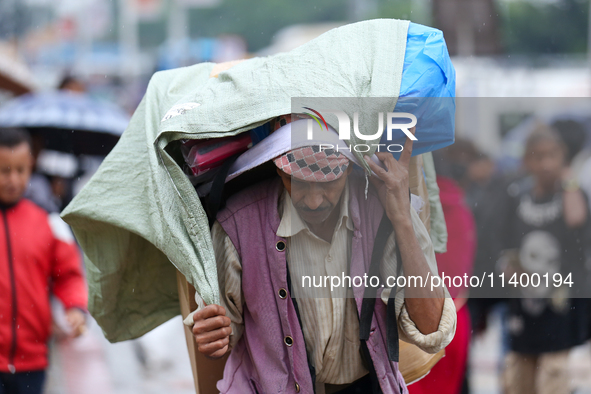 A daily wage worker is covering himself and his loads with sacks and plastic as he walks through the rain in Kathmandu, Nepal, on July 11, 2...