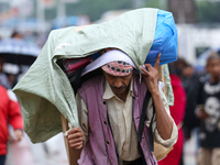 A daily wage worker is covering himself and his loads with sacks and plastic as he walks through the rain in Kathmandu, Nepal, on July 11, 2...