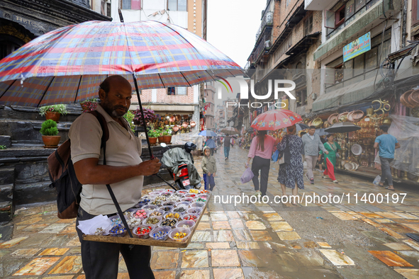 A Nepali vendor is taking shelter under an umbrella as he sells decorations in Kathmandu, Nepal, on July 11, 2024. Nepal is recording heavy...