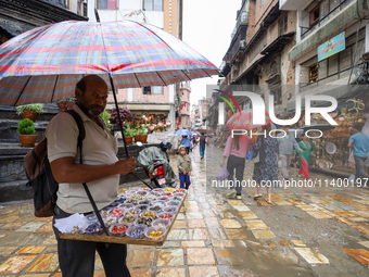 A Nepali vendor is taking shelter under an umbrella as he sells decorations in Kathmandu, Nepal, on July 11, 2024. Nepal is recording heavy...