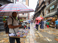 A Nepali vendor is taking shelter under an umbrella as he sells decorations in Kathmandu, Nepal, on July 11, 2024. Nepal is recording heavy...