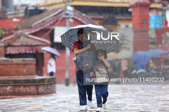 An elder and younger sister duo are taking shelter under an umbrella as they return home from school amidst the rain in Kathmandu, Nepal, on...