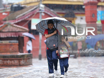 An elder and younger sister duo are taking shelter under an umbrella as they return home from school amidst the rain in Kathmandu, Nepal, on...