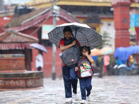 An elder and younger sister duo are taking shelter under an umbrella as they return home from school amidst the rain in Kathmandu, Nepal, on...