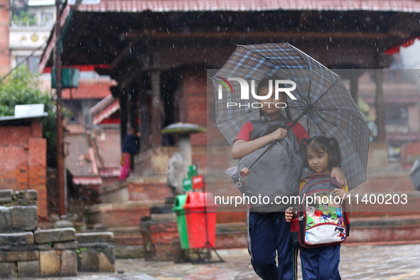 An elder and younger sister duo are taking shelter under an umbrella as they return home from school amidst the rain in Kathmandu, Nepal, on...