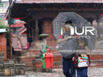 An elder and younger sister duo are taking shelter under an umbrella as they return home from school amidst the rain in Kathmandu, Nepal, on...