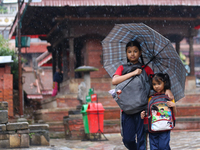 An elder and younger sister duo are taking shelter under an umbrella as they return home from school amidst the rain in Kathmandu, Nepal, on...