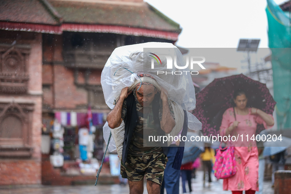 A daily wage worker is covering himself and his loads with sacks and plastic as he walks through the rain in Kathmandu, Nepal, on July 11, 2...