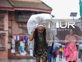 A daily wage worker is covering himself and his loads with sacks and plastic as he walks through the rain in Kathmandu, Nepal, on July 11, 2...