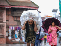 A daily wage worker is covering himself and his loads with sacks and plastic as he walks through the rain in Kathmandu, Nepal, on July 11, 2...