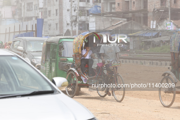 A boy is riding on a rickshaw on a dusty road in Dhaka, Bangladesh, on July 11, 2024, after returning from school. 