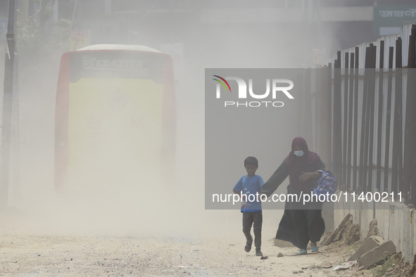 A boy is coming back from school with his mother on a dusty road in Dhaka, Bangladesh, on July 11, 2024. 