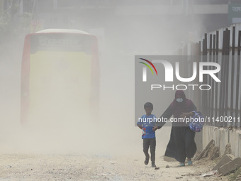 A boy is coming back from school with his mother on a dusty road in Dhaka, Bangladesh, on July 11, 2024. (