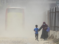 A boy is coming back from school with his mother on a dusty road in Dhaka, Bangladesh, on July 11, 2024. (