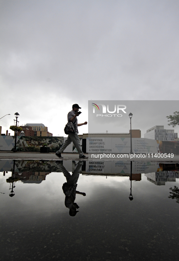 A pedestrian is walking downtown reflected in a puddle of water in Brampton, Ontario, on July 11, 2024. Remnants of Hurricane Beryl are pass...