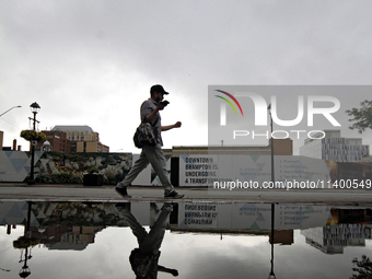 A pedestrian is walking downtown reflected in a puddle of water in Brampton, Ontario, on July 11, 2024. Remnants of Hurricane Beryl are pass...