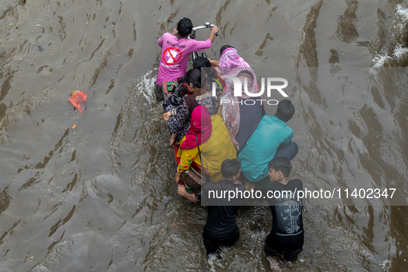 People are wading through a waterlogged street after heavy rain in Dhaka, Bangladesh, on July 12, 2024. 