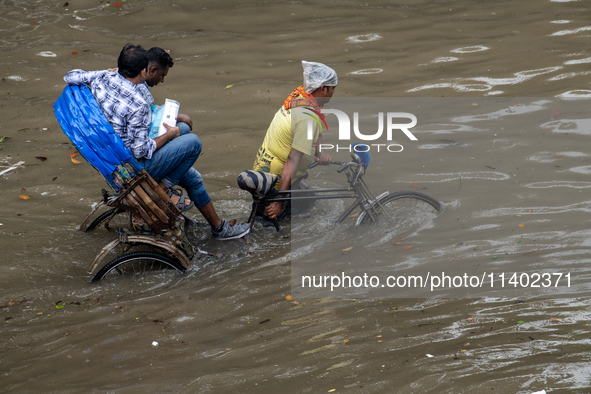 Passengers are riding on a rickshaw to go through a waterlogged street after heavy rain in Dhaka, Bangladesh, on July 12, 2024. 