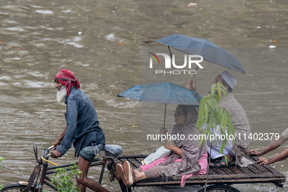 Passengers are riding on a rickshaw to go through a waterlogged street after heavy rain in Dhaka, Bangladesh, on July 12, 2024. 